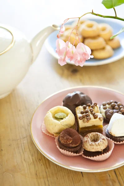 Тарелки с выпечкой, печеньем и чайником на деревянном столе — стоковое фото