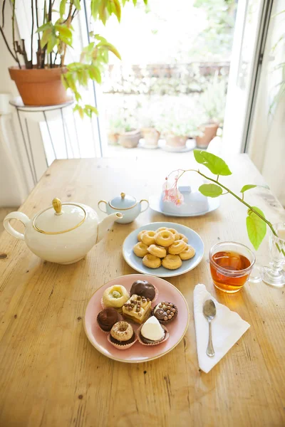 Plates of pastries and biscuits and tea pot on wooden table — Stock Photo, Image