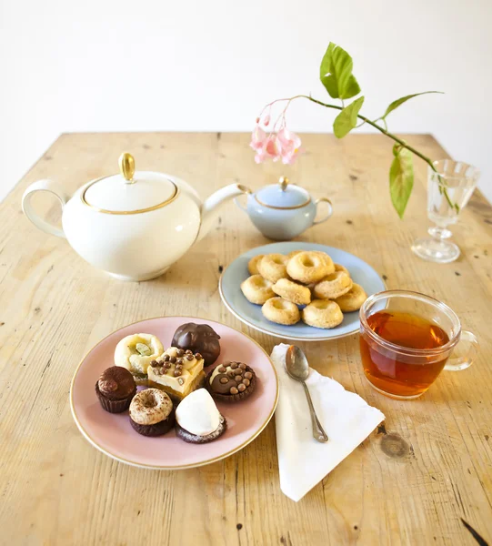 Platen van gebakjes en koekjes en theepot op houten tafel — Stockfoto