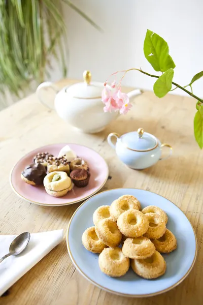 Plates of pastries and biscuits and tea pot on wooden table — Stock Photo, Image