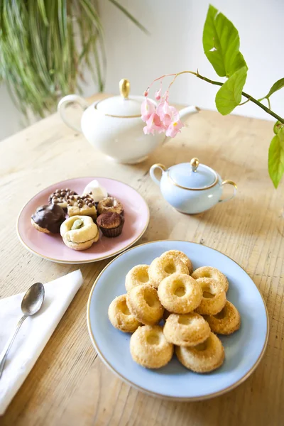 Platen van gebakjes en koekjes en theepot op houten tafel — Stockfoto
