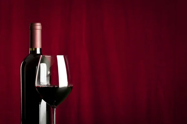 A glass of red wine and a bottle on red background — Stock Photo, Image