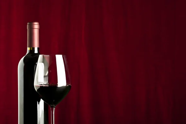 A glass of red wine and a bottle on red background — Stock Photo, Image