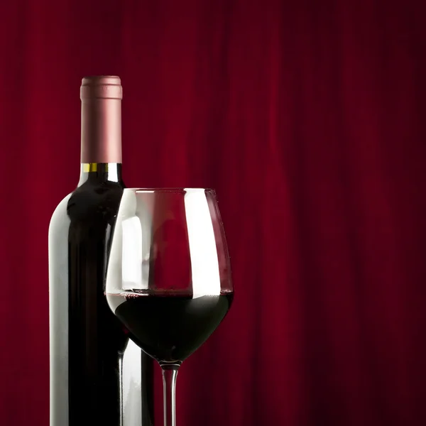 Ein Glas Rotwein und eine Flasche auf rotem Hintergrund — Stockfoto