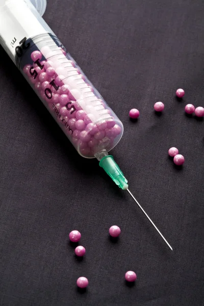 Syringe filled with pink candy on a black background — Stock Photo, Image