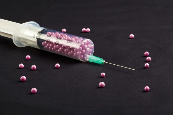 Syringe filled with pink candy on a black background — Stock Photo, Image