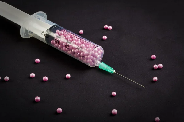 Syringe filled with pink candy on a black background — Stock Photo, Image