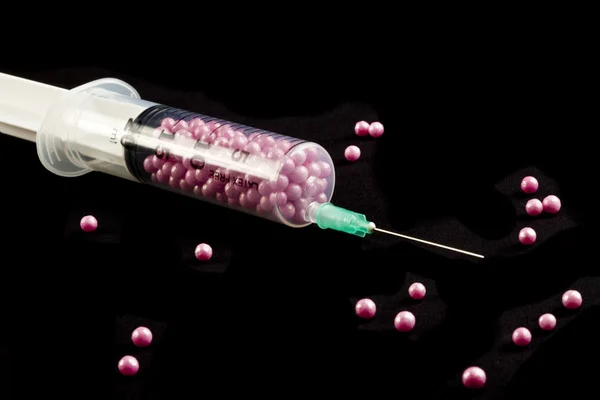 Syringe filled with pink candy on a black background — Stock Photo, Image