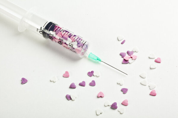 Syringe filled with heart shaped candy on a white background