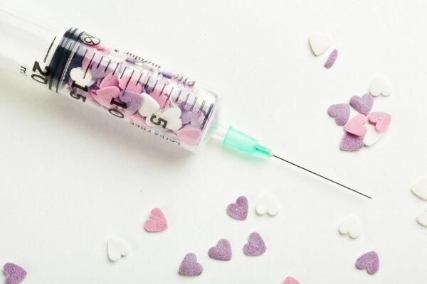Syringe filled with heart shaped candy on a white background
