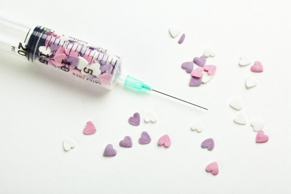 Syringe filled with heart shaped candy on a white background