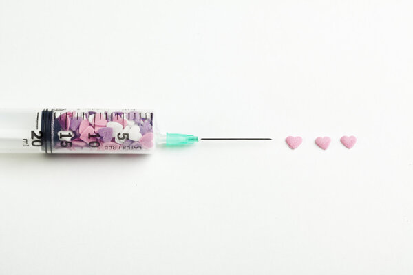 Syringe filled with heart shaped candy on a white background