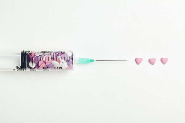Syringe filled with heart shaped candy on a white background