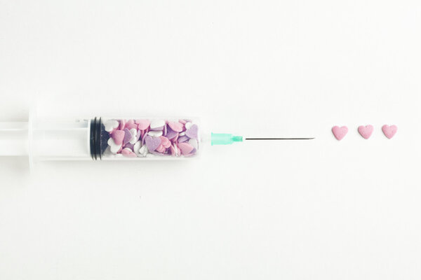 Syringe filled with heart shaped candy on a white background
