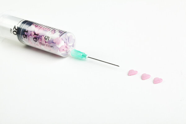 Syringe filled with heart shaped candy on a white background