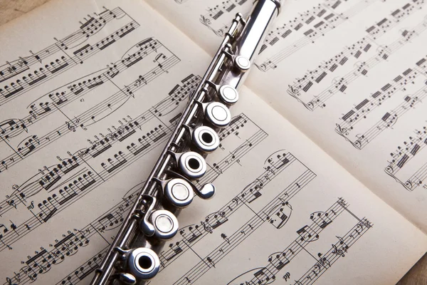 Silver flute on an ancient music score background — Stock Photo, Image