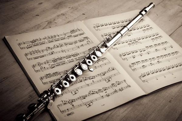 Silver flute on an ancient music score background — Stock Photo, Image