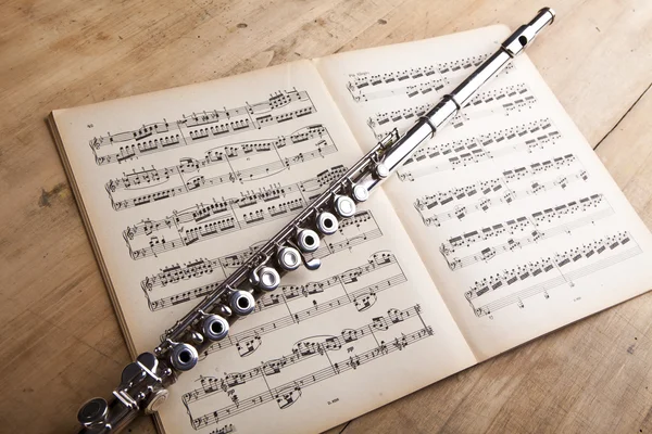 Stříbrná flétna na pozadí staré hudby skóre — Stock fotografie
