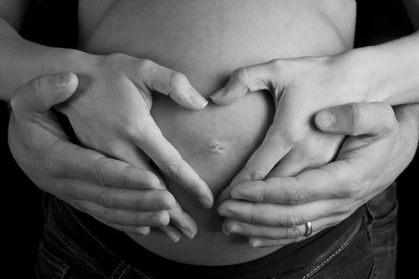 Руки беременной женщины и ее мужа в форме сердца на ней быть — стоковое фото