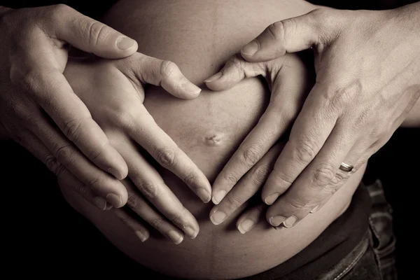 Ręce kobiety w ciąży i jej mąż w kształcie serca na nią być — Zdjęcie stockowe