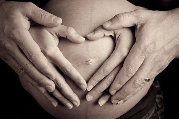 Hands of pregnant woman and her husband in heart shape on her be — Stock Photo, Image