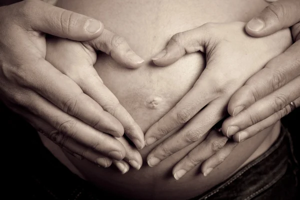 Hands of pregnant woman and her husband in heart shape on her be — Stock Photo, Image