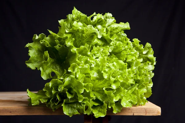 Fresh green lettuce on wooden table on black background — Stock Photo, Image