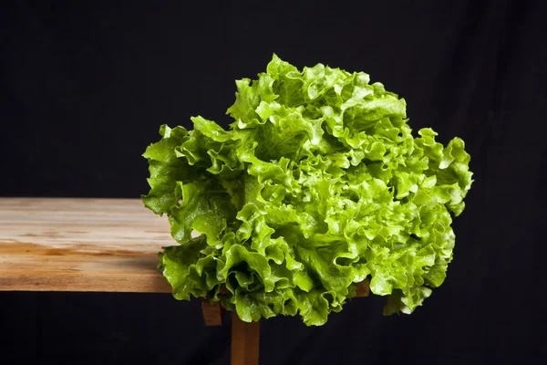 Fresh green lettuce on wooden table on black background — Stock Photo, Image