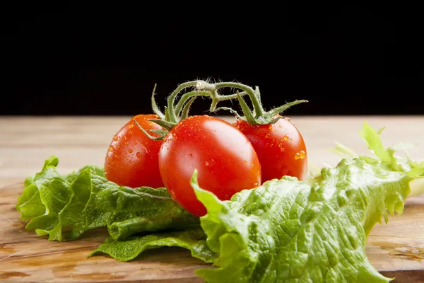 Fresh ripe cherry tomato and lettuce on wooden table — Stock Photo, Image