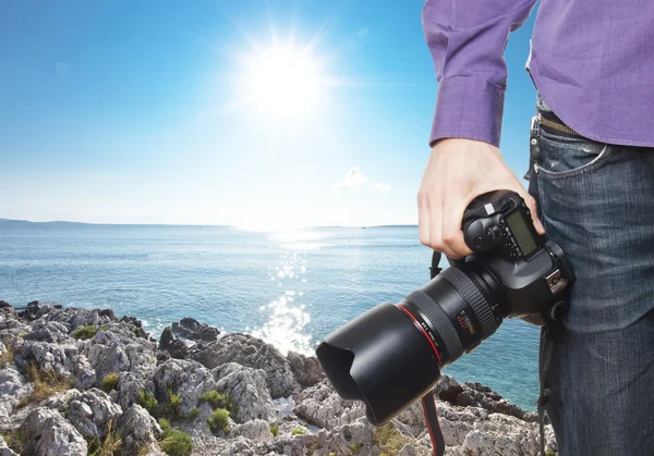 Photographer's hand holding professional digital camera on rocky — Stock Photo, Image