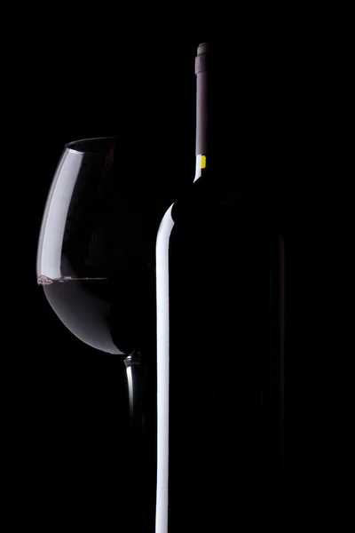 Vidro elegante e garrafa de vinho tinto no fundo preto — Fotografia de Stock