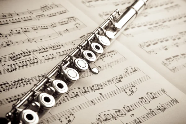 Silver flute on an ancient music score background Stock Photo