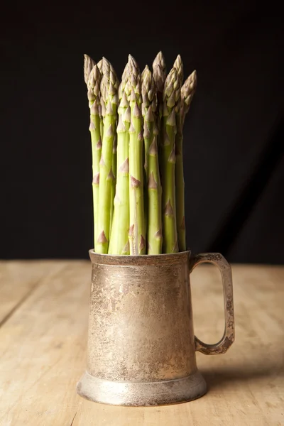 Bunch of fresh green asparagus in a mug on wooden table — Stock Photo, Image
