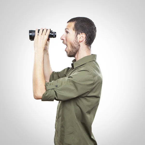 Mladý muž dívá dalekohledem, výraz obličeje překvapení — Stock fotografie