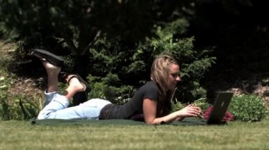 A young woman uses her laptop outside in the park