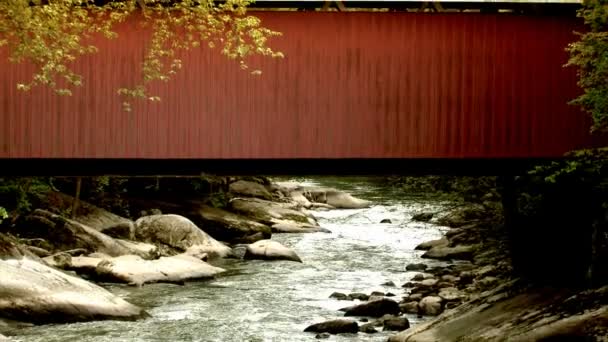 Un puente cubierto de rojo sobre un arroyo que fluye — Vídeo de stock