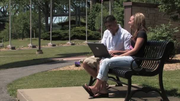 Um jovem casal usa um laptop sem fio no exterior do parque — Vídeo de Stock