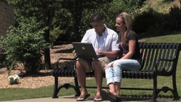 Молодая пара использует беспроводной ноутбук снаружи в парке — стоковое видео