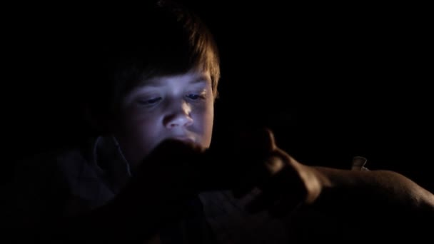 Ένα νεαρό αγόρι που παίζει ένα βιντεοπαιχνίδι χειρός στο σκοτάδι. — Αρχείο Βίντεο