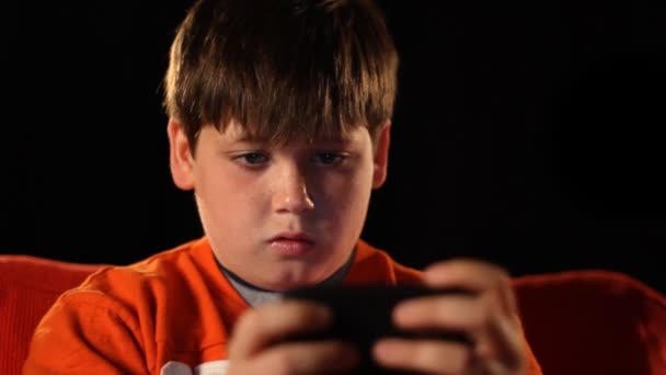 Ένα νεαρό αγόρι που παίζει ένα βιντεοπαιχνίδι χειρός στο σκοτάδι. — Αρχείο Βίντεο