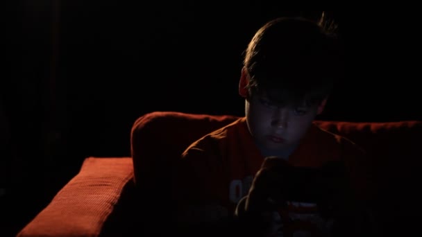 Um menino joga um jogo de vídeo portátil no escuro . — Vídeo de Stock