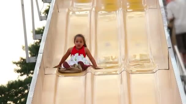 Uma menina desliza para baixo de um grande slide em um carnaval . — Vídeo de Stock