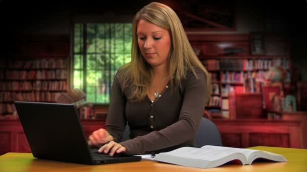 Una chica en edad universitaria hace los deberes en la biblioteca con un portátil . — Vídeos de Stock
