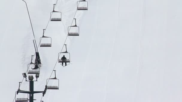 Gli sciatori cavalcano uno skit lift fino alla cima di una montagna innevata . — Video Stock