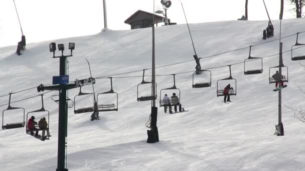 Gli sciatori cavalcano uno skit lift fino alla cima di una montagna innevata . — Video Stock