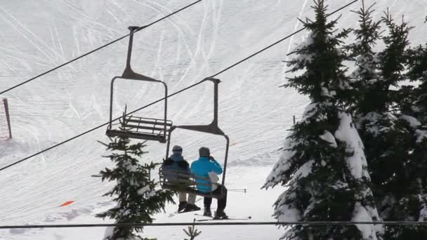 Skifahrer fahren mit dem Skilift auf den Gipfel eines verschneiten Berges. — Stockvideo