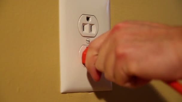 Close-up shot of a man plugging and unplugging an orange electrical cord into a U.S. wall outlet.