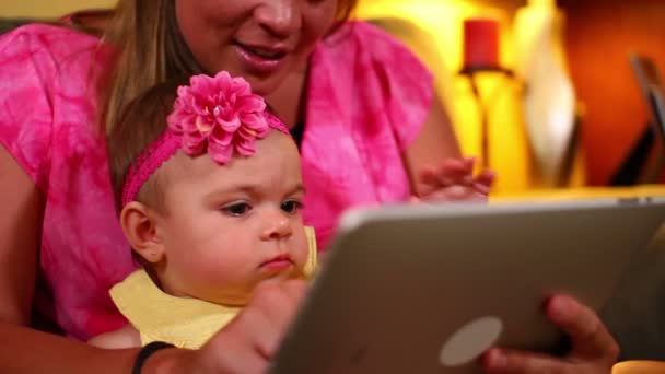 Uma mãe usa um computador tablet com seu bebê no sofá . — Vídeo de Stock