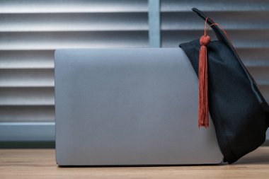 Tahta masa arkasında mezuniyet şapkası ve dizüstü temposu