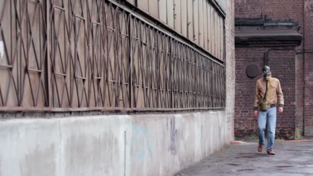 De man in het masker gas loopt langs de stoffige fabriek muur — Stockvideo